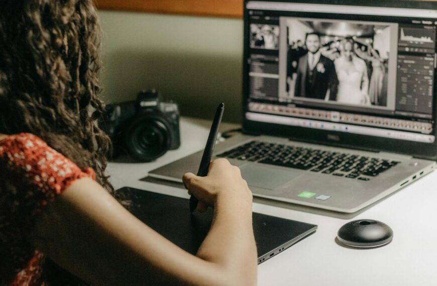 A woman editing wedding photos on a tablet using a laptop, representing modern graphic design work.