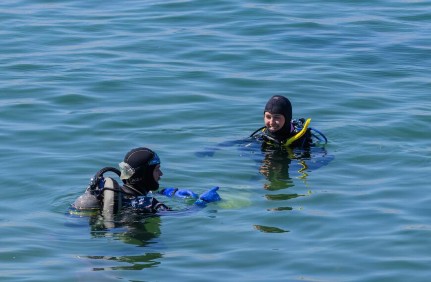 Two scuba divers enjoying a sunny day in clear open water, equipped with full scuba gear.