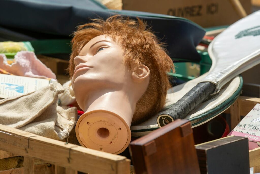 Close-up of mannequin head and items at a flea market, showcasing various objects like a tennis racket.