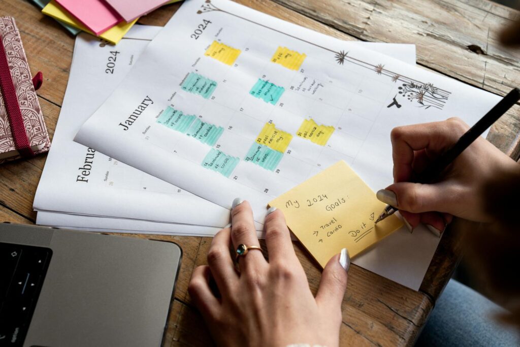 Close-up of a person writing new year's goals on a sticky note with a 2024 calendar in the background.