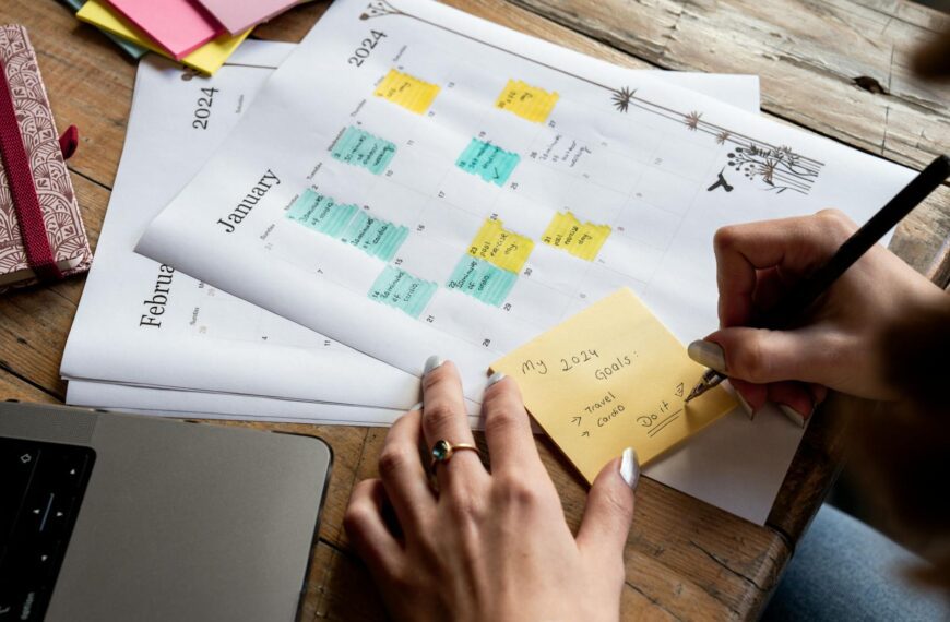 Close-up of a person writing new year's goals on a sticky note with a 2024 calendar in the background.