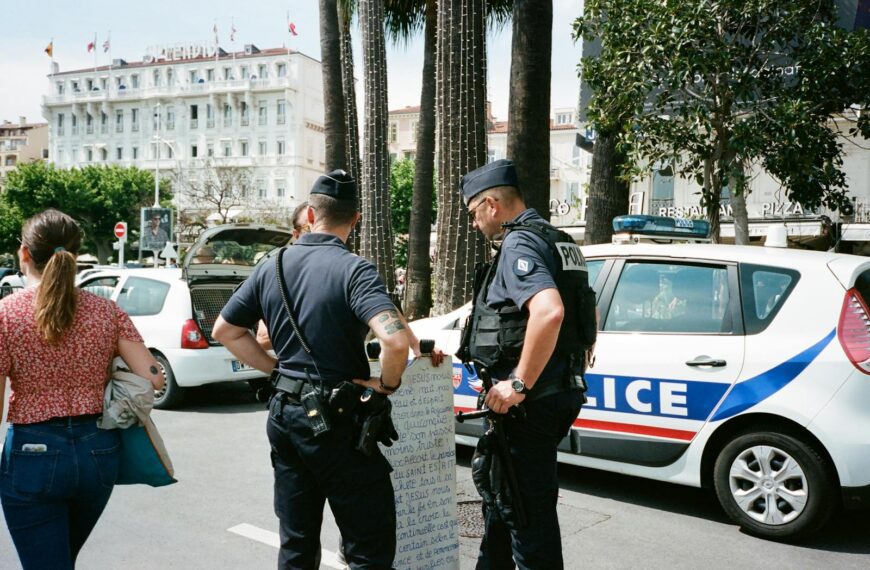 Police officers and a civilian interact near a police car on a busy city street.