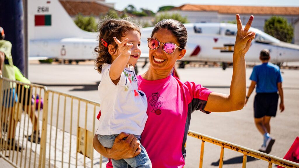 Happy mother and daughter posing with peace signs outdoors on a sunny day.