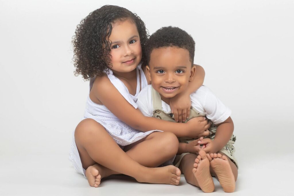 Charming studio portrait of young siblings sitting together and smiling warmly.