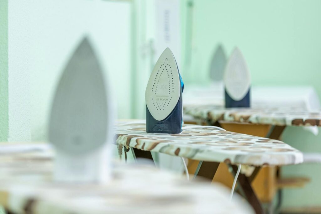 Close-up of modern irons placed on ironing boards with camouflage pattern covers in a bright indoor setting.