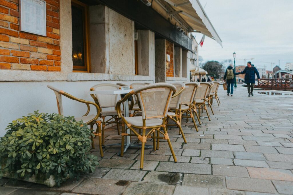 Outdoor wicker chairs line a cozy European café with a cobblestone street, perfect for a relaxing day out.