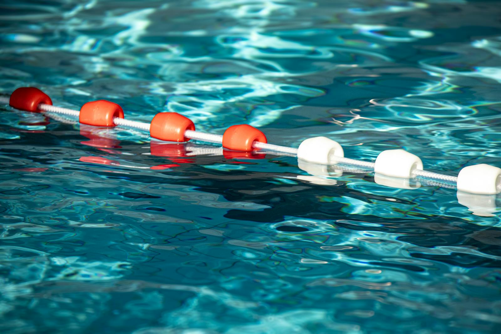 Colorful pool buoys creating striking contrast on rippled blue water surface.