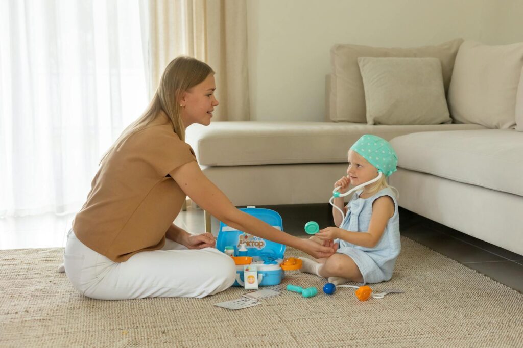 A mother and daughter play with a toy doctor kit in a cozy living room setting.