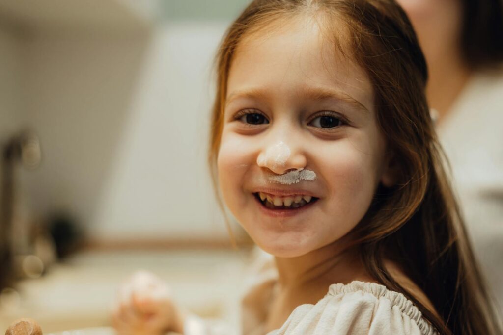 Cute girl with flour on her nose smiling in a cozy kitchen setting.