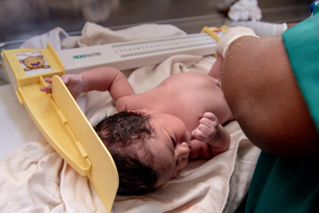 A newborn baby is weighed by a healthcare worker in a hospital setting. Captured close-up.