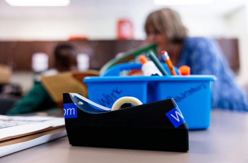 A focused shot of a tape dispenser and school supplies in a classroom environment.