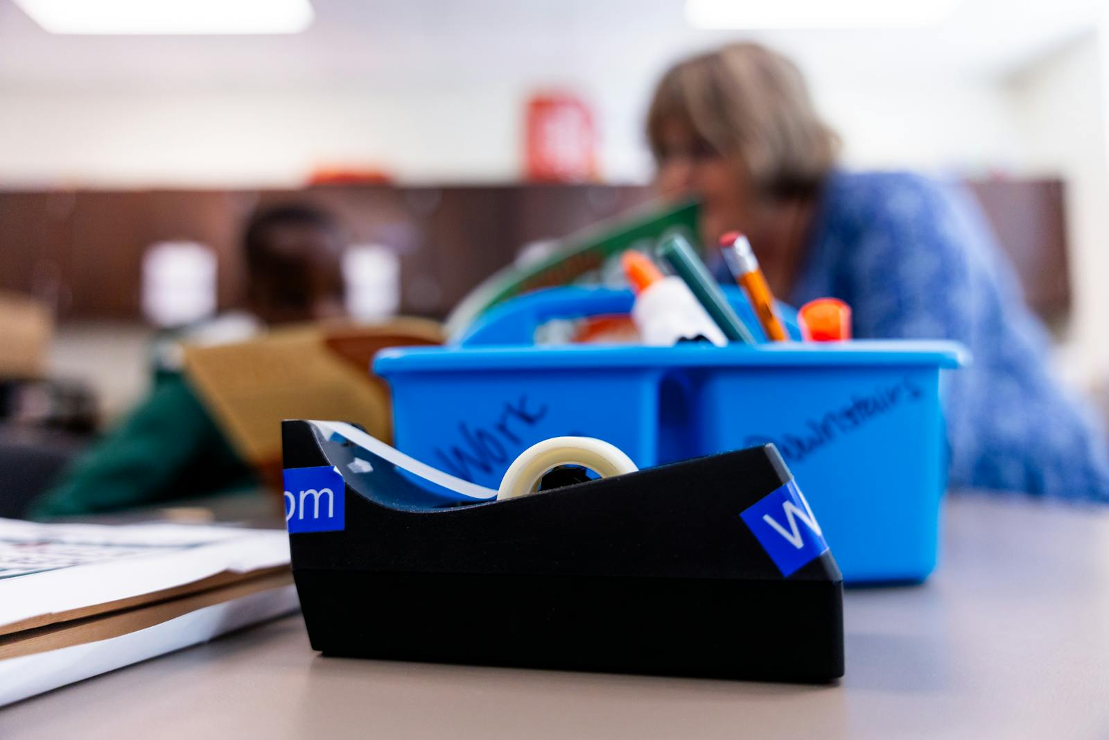 A focused shot of a tape dispenser and school supplies in a classroom environment.