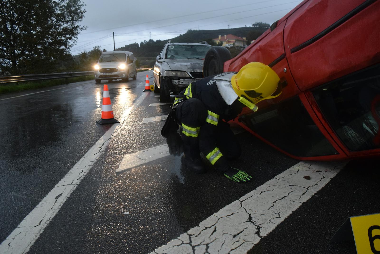 Firefighter attending to an overturned car on a rainy road in Póvoa de Lanhoso, Braga, Portugal.