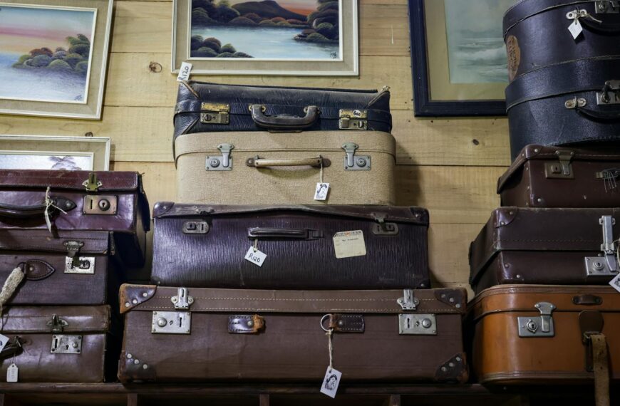 A collection of vintage suitcases stacked in an antique store with framed art on the wall.