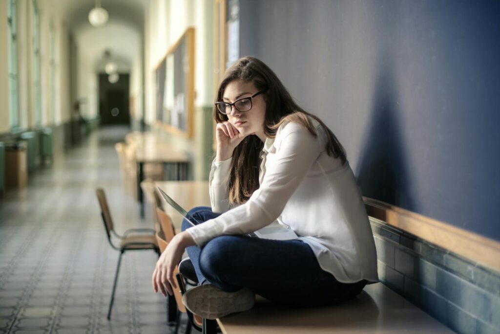 Thoughtful woman sitting alone in a school hallway contemplating problems.