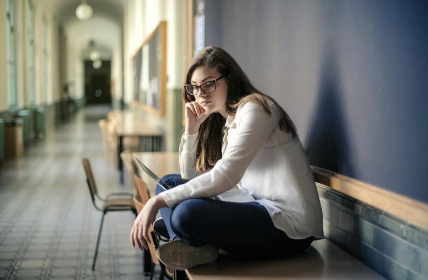 Thoughtful woman sitting alone in a school hallway contemplating problems.