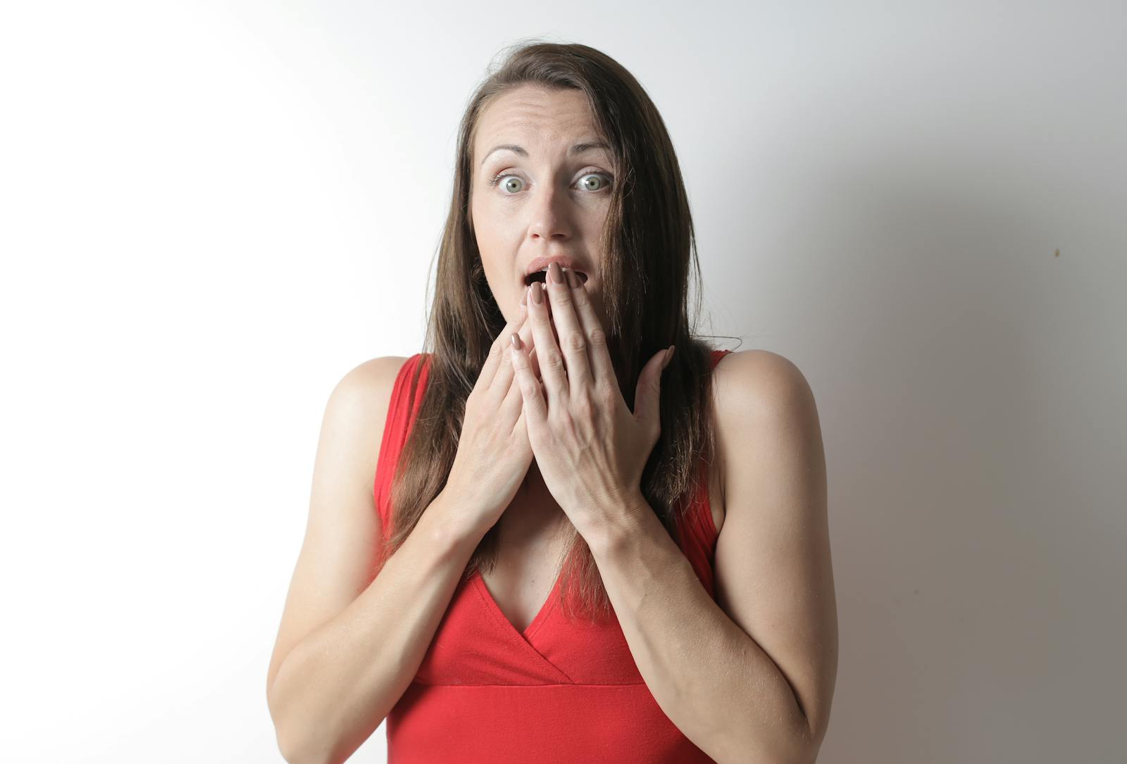 A surprised young woman in a red dress reacting dramatically against a plain white background.