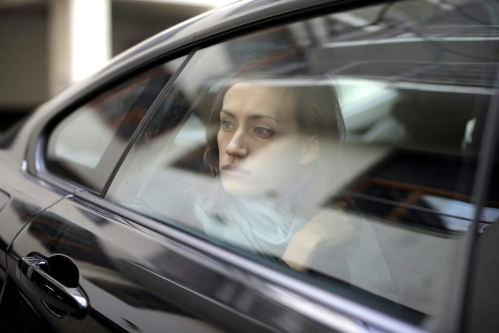 A thoughtful woman gazes out of a car window, lost in contemplation, conveying deep emotions.