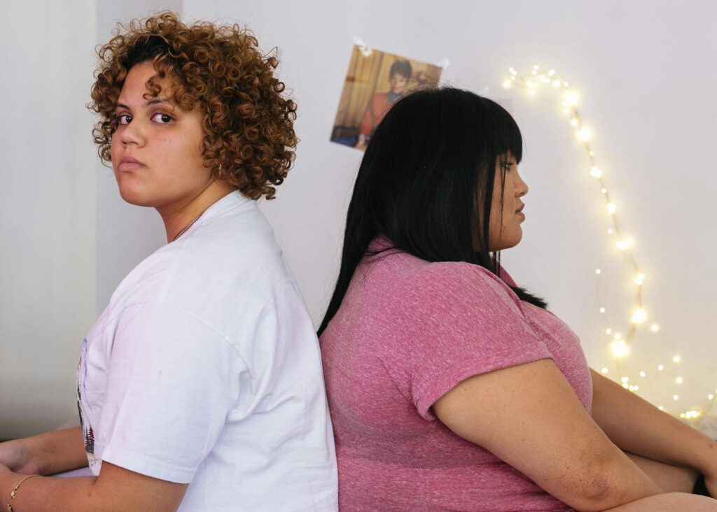 Two women sitting back to back indoors, conveying tension or disagreement.