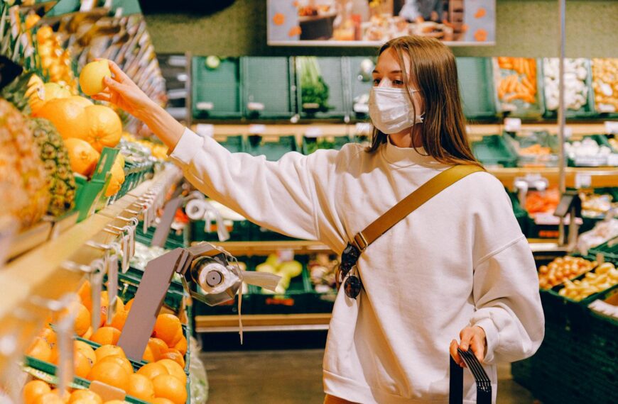 Woman wearing a mask selecting fruit at a grocery store during pandemic.