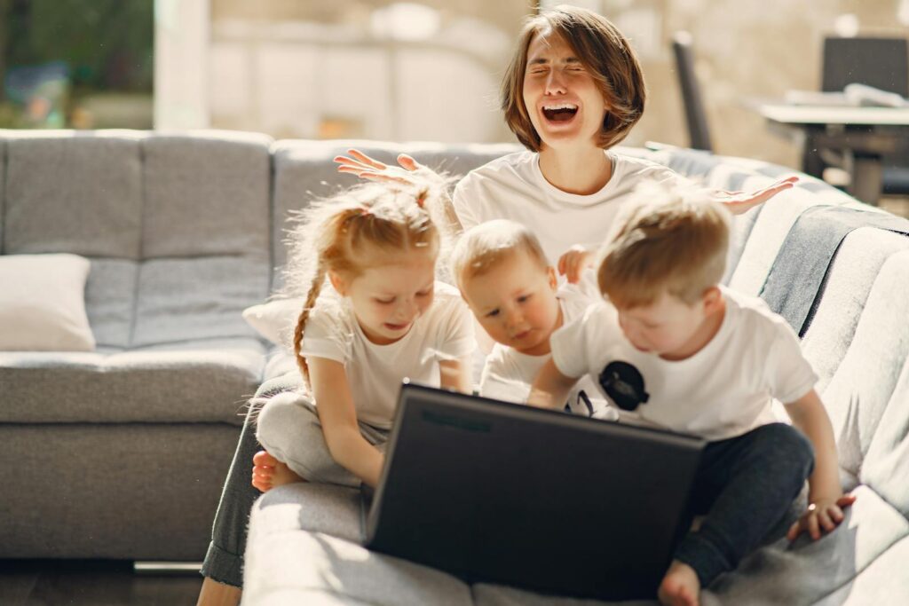 Stressed woman asking for help while sitting with small children playing on laptop together on sofa in living room