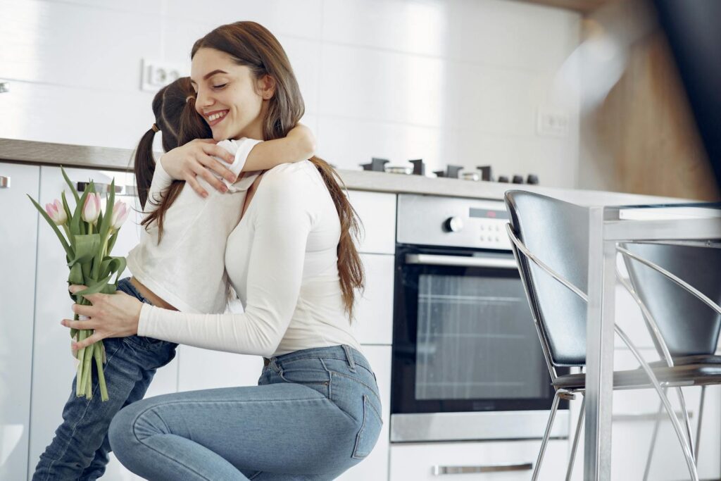 A joyful mother-daughter hug in a modern kitchen, holding tulips.