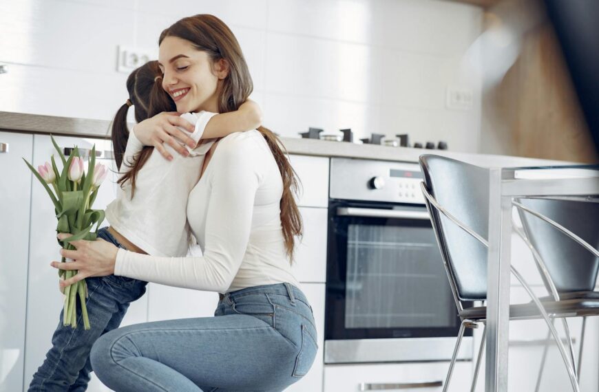A joyful mother-daughter hug in a modern kitchen, holding tulips.