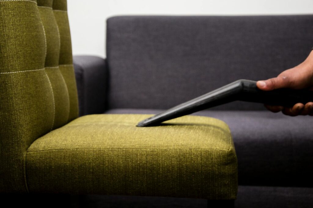 Close-up of a person vacuuming a modern sofa chair indoors, highlighting cleaning service.