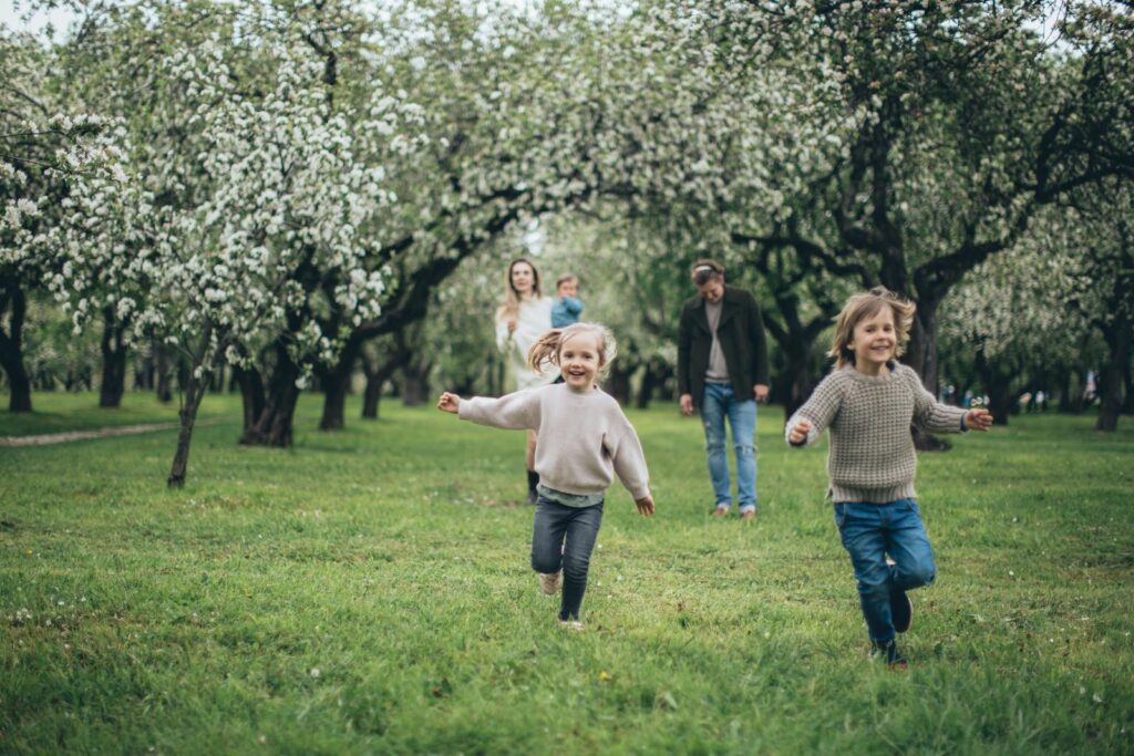 A happy family running and playing among blooming trees in a lush green park during spring.