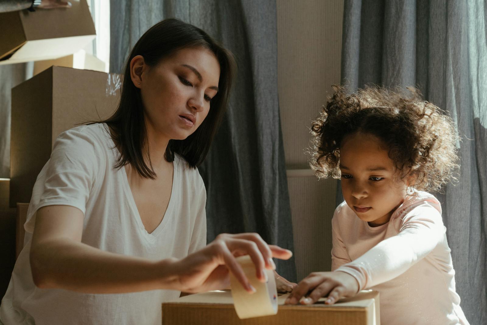 A young mother and her daughter packing moving boxes in their new home.