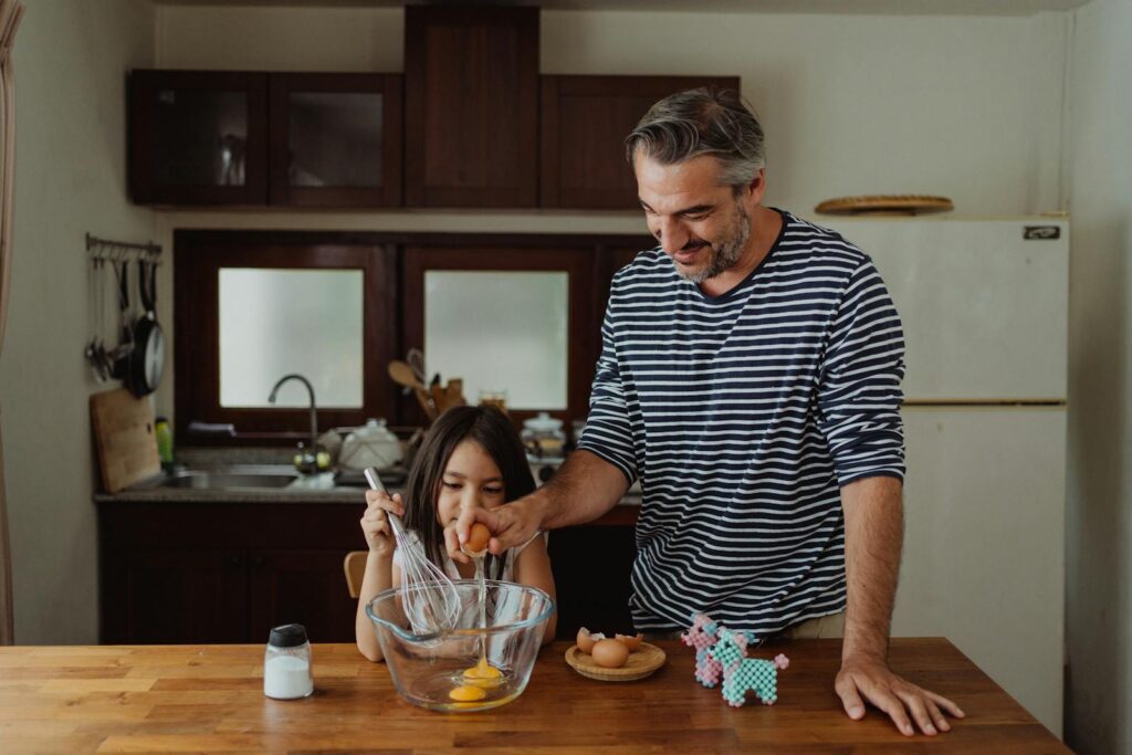 Father and daughter cracking eggs while baking in a cozy kitchen, capturing family bonding and cooking moments.