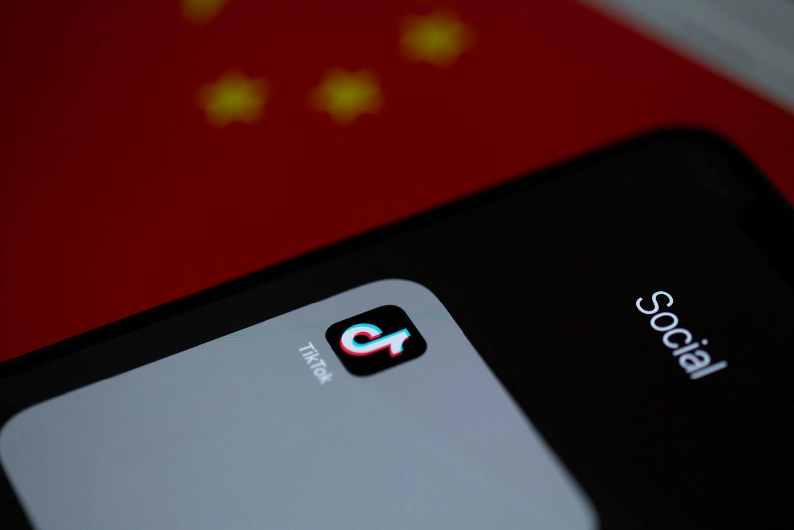 Close-up of TikTok app icon on a smartphone, set against a Chinese flag background.