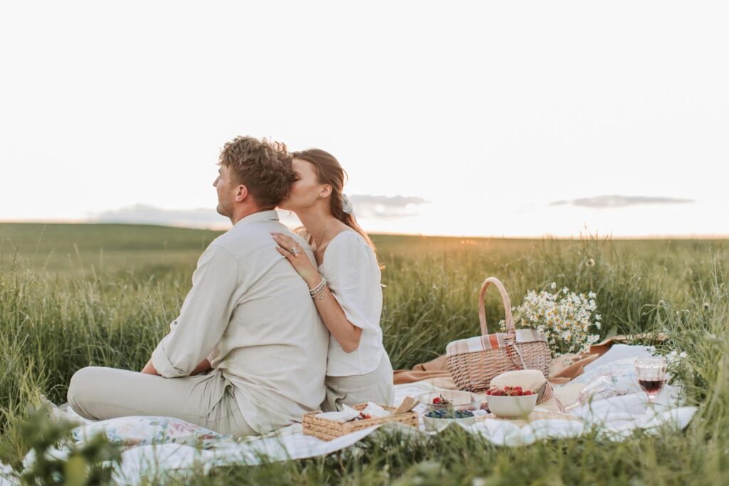 Couple enjoying a romantic picnic in a serene field at sunset, capturing love and tranquility.