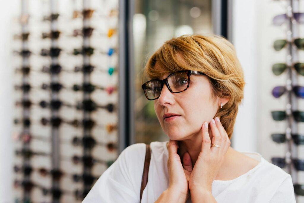 Woman examining new eyewear in store with diverse eyeglasses selection in the background.