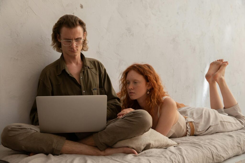 Couple lounging indoors and browsing on a laptop, creating a cozy and modern atmosphere.