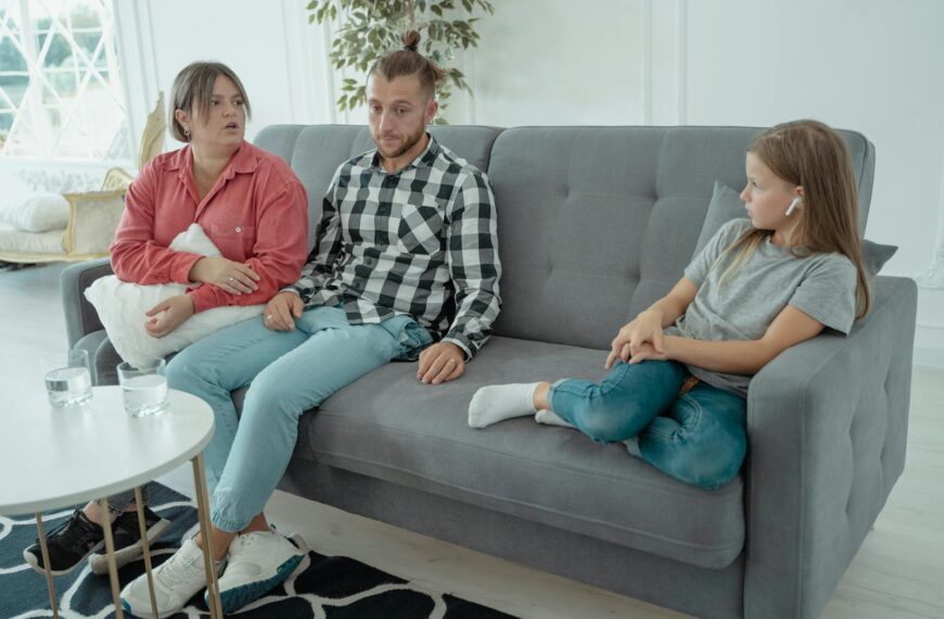 A family sits together on a sofa, discussing in a comfortable home setting, indicating a counseling session.