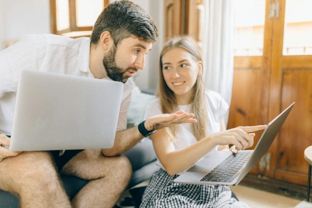 Young couple sitting together, discussing something on their laptops in a cozy room.