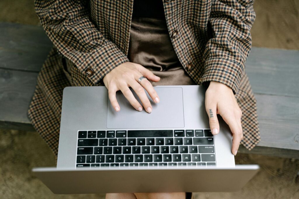 High angle view of individual using a laptop on a wooden bench while wearing a checkered coat.