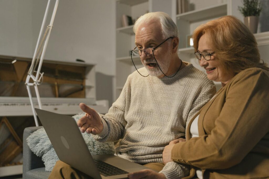 Senior couple smiling and gesturing during a video call on a laptop at home.