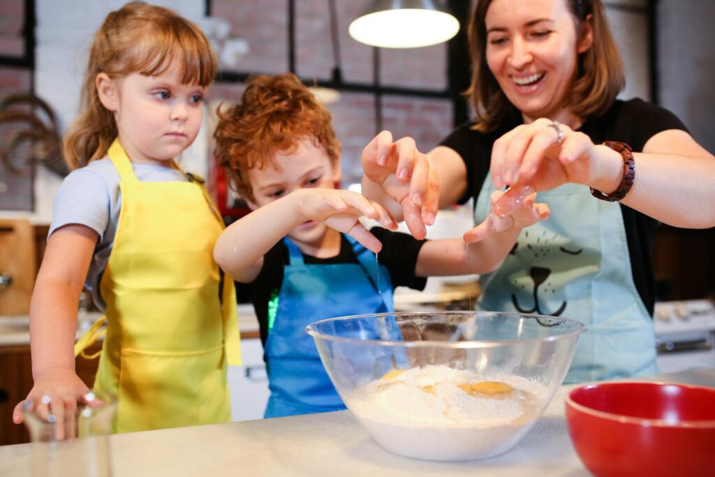 Children and a woman joyfully baking cookies together, learning cooking skills.