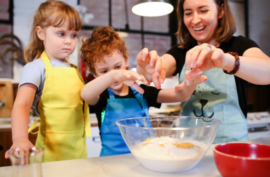 Children and a woman joyfully baking cookies together, learning cooking skills.