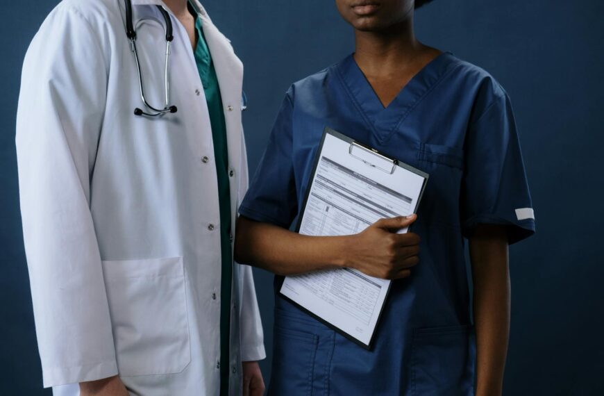 Two healthcare professionals in scrubs and lab coat with a clipboard, representing teamwork.