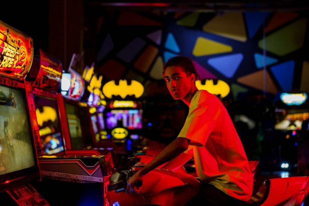 A young adult plays an arcade game in a vibrant, illuminated gaming center.