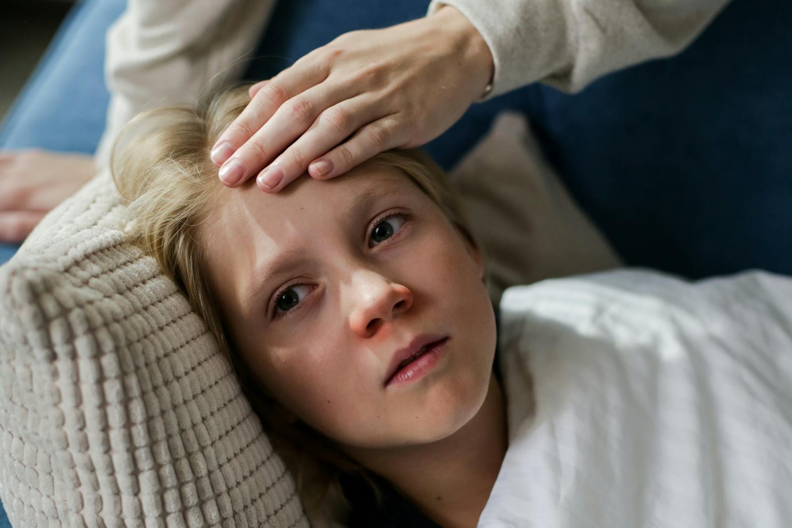 Young child lying down with a hand checking for fever, indicating illness or flu symptoms.