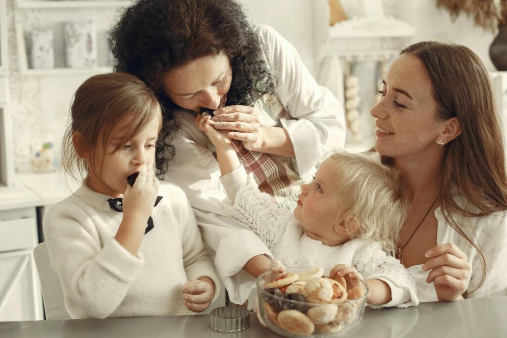 Grandmother, mother, and daughters enjoying baking cookies together in cozy kitchen setting.