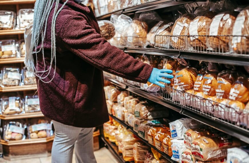 Side view of crop anonymous female customer picking loaf of bread in supermarket during coronavirus epidemic