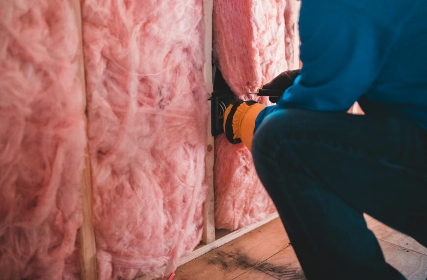 Focused worker installing pink fiberglass insulation in a building interior.