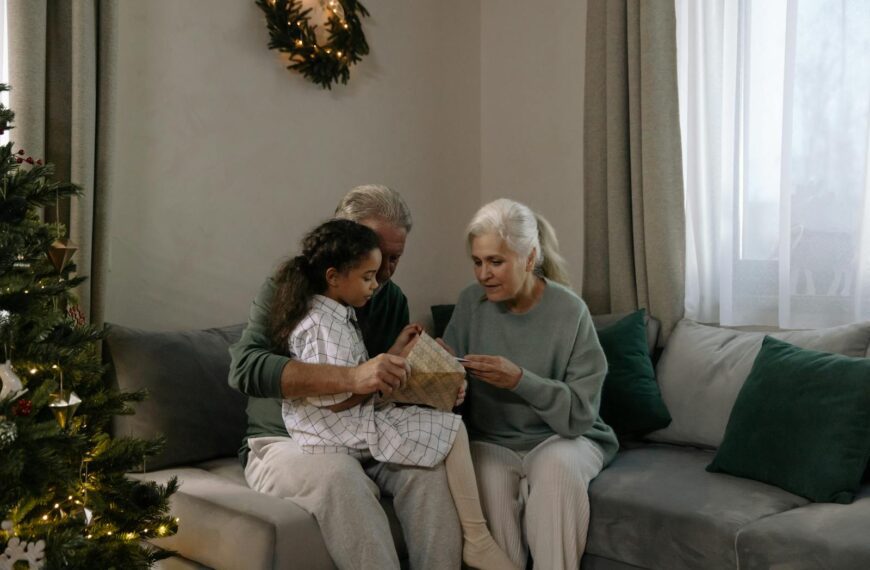 A happy family moment with grandparents and granddaughter opening a Christmas gift together.