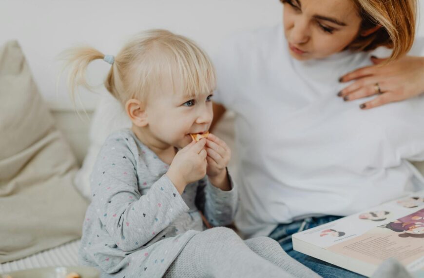 A young mother and her daughter share a tender moment while having a snack indoors.