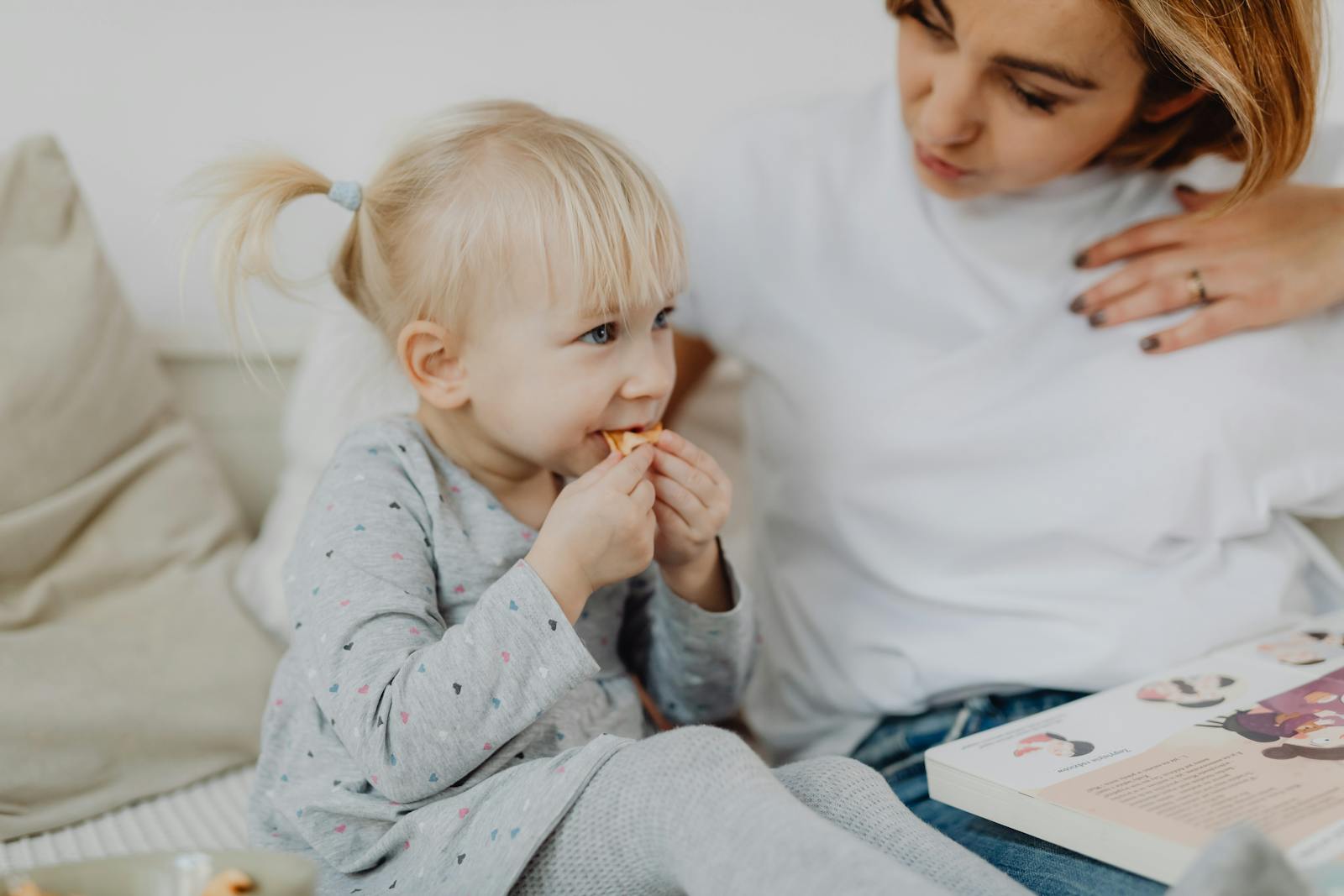 A young mother and her daughter share a tender moment while having a snack indoors.